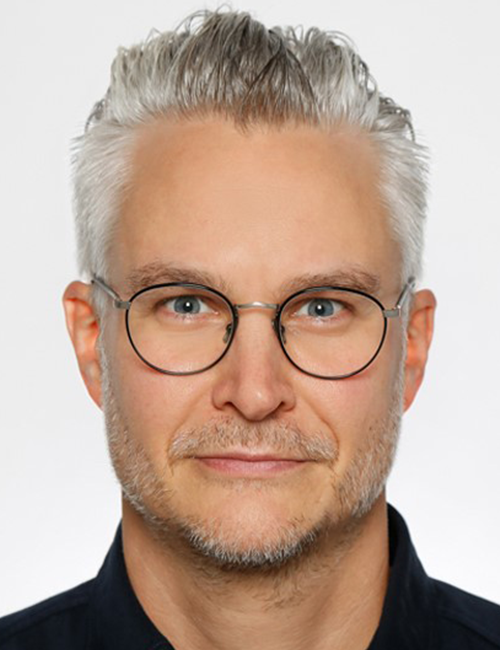 Porträtbild von Florian Brauch. Er trägt kurze graue Haare und eine größere, runde Brille mit schwarzem Rahmen. Er blickt freundlich und direkt in die Kamera.